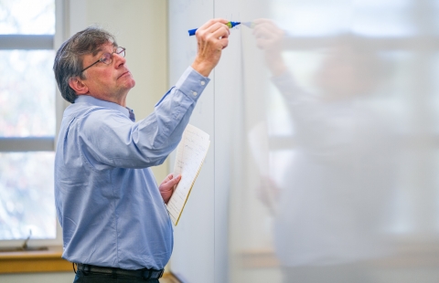 A photo of a professor writing on a whiteboard
