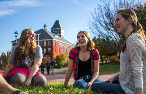 Three female college students sitting in the grass laughing